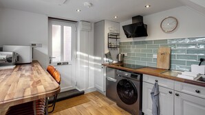 A modern kitchen with a wooden dining table, built-in appliances, and a green-tiled backsplash.