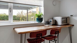 A small kitchen with a wooden countertop, two red chairs, a microwave, and a potted plant.
