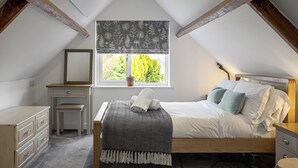 A bedroom with a bed, bedside table, dresser, and a window with a view of greenery.