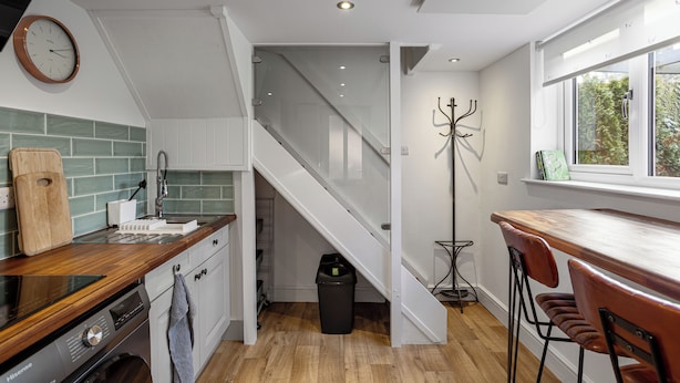 A modern kitchen with a wooden countertop, a built-in oven, and a sink. There is a staircase leading to a loft area with a glass railing.