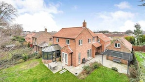 A large brick house with a conservatory, a garden, and a neighboring house.