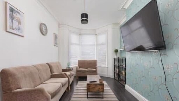 A living room with a sofa, armchairs, a coffee table, and a flat-screen TV mounted on the wall.