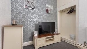 A room with a patterned wallpaper, a television on a wooden stand, a wardrobe, and a coat rack.
