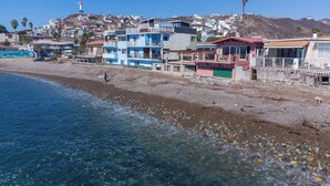A coastal town with buildings along the beach, clear blue water, and a lighthouse in the background.