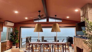 A dining area with a view of the sea, a ceiling fan, and a television on a stone wall.