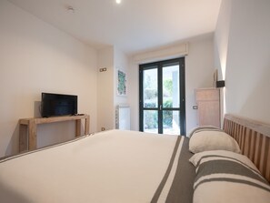 Une chambre à coucher avec un lit, un téléviseur posé sur un meuble en bois, un radiateur et une fenêtre donnant sur un paysage verdoyant.