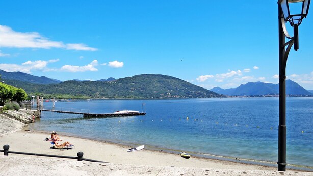 A beach with a pier extending into calm waters, surrounded by hills. - Baveno View by Interhome (Baveno)