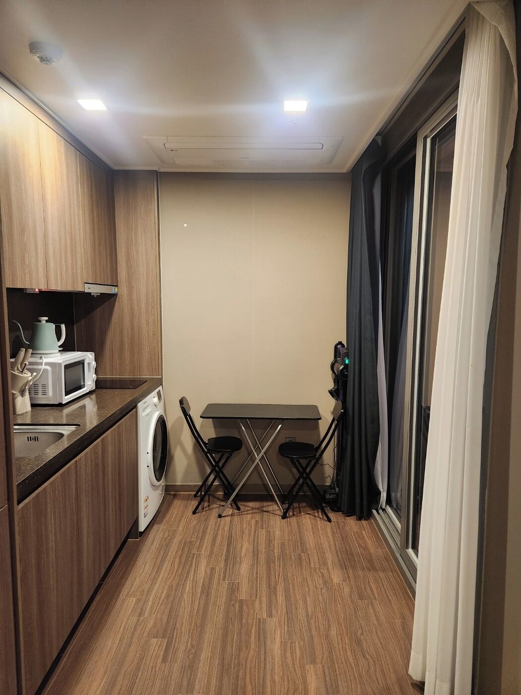 A compact kitchen with a washing machine, microwave, and a small table with chairs.