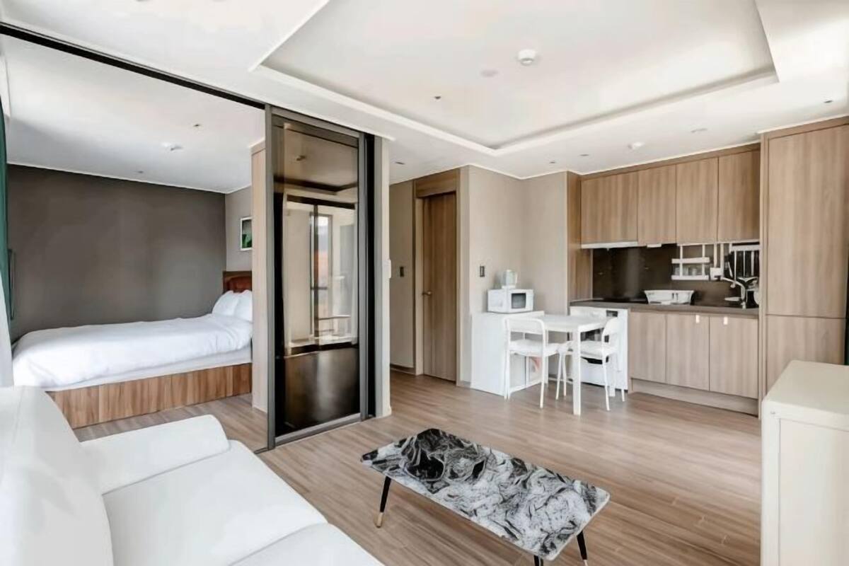 Quarto de hotel moderno com cama, sofá, área de refeições e cozinha compacta.