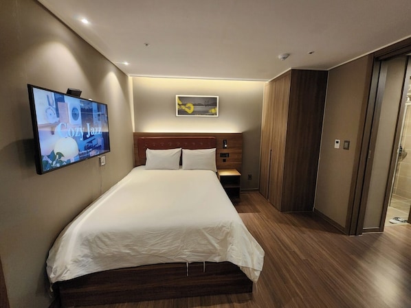 A modern hotel room with a large bed, a flat-screen TV mounted on the wall, a wooden headboard, and a small bedside table. - A1 with Haeundae (Busan)
