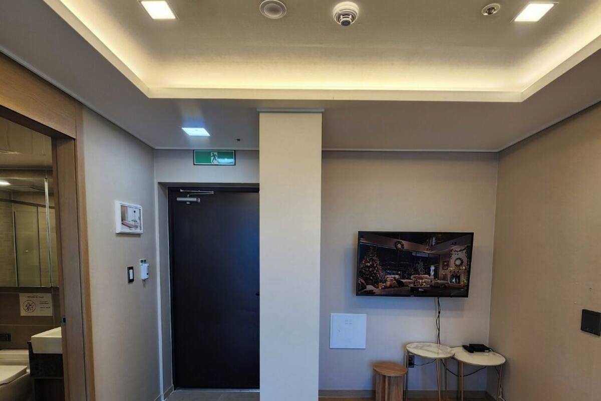 Um hall de hotel moderno com piso de madeira, um pilar grande, um balcão de recepção e uma televisão montada na parede.