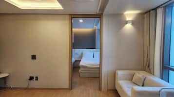 A modern hotel room with a wooden floor, a sofa, a bed, and a large window with curtains.