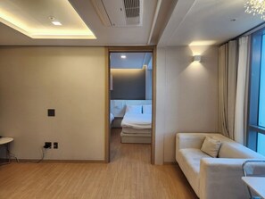 Una habitación de hotel moderna con suelo de madera, un sofá, una cama y un gran ventanal con cortinas.