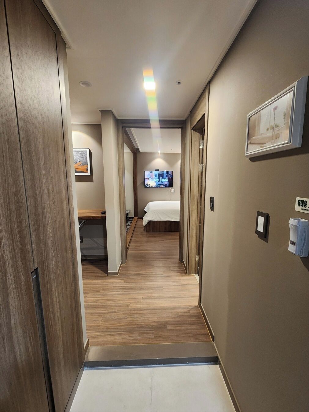 A hotel hallway with a bed, a TV, and a trash bin.