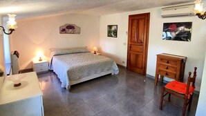 A bedroom with a bed, bedside tables, a wooden dresser, a chair, and wall-mounted artwork. - La Favola by Interhome (Ischia)