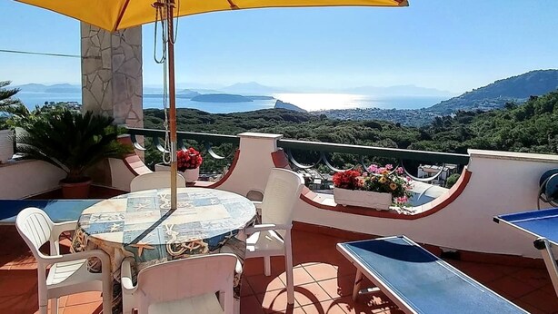 A terrace with a table and chairs, a yellow umbrella, and a view of the sea and mountains. - La Favola by Interhome (Ischia)