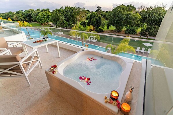 Zona de piscina en la azotea con jacuzzi, sillas de descanso y barandilla de cristal con vistas a un jardín exuberante.