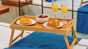 Ein Frühstückswagen mit Croissants, einer Beeren-Schüssel und zwei Gläsern Orangensaft auf einem Bett mit einem blauen Handtuch.