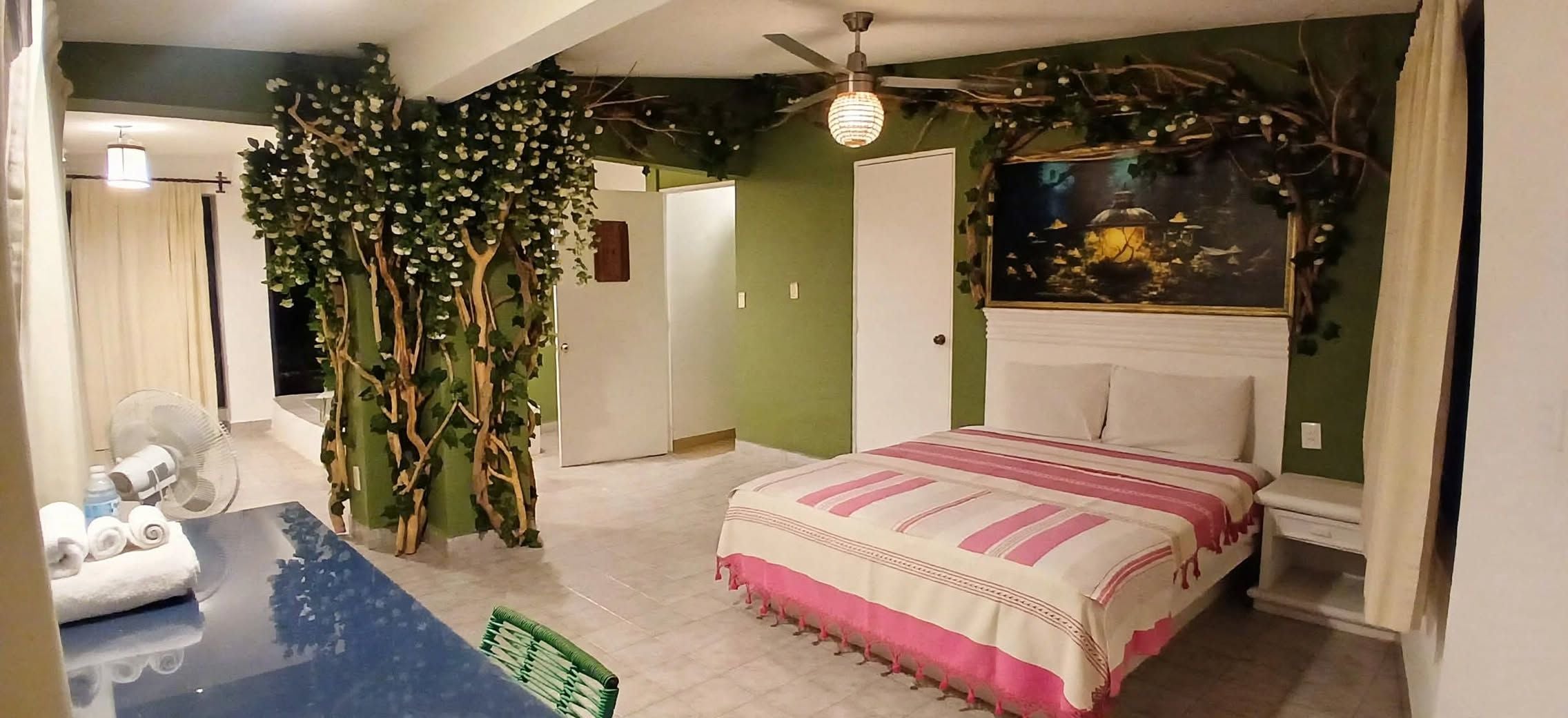 Ein Schlafzimmer mit einem Bett, einem Ventilator, einer grünen Wand und Deckenventilator.