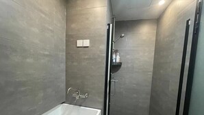A modern bathroom with a bathtub, a glass-enclosed shower, and a shelf with toiletries. - 2mins walk to Metro station(3 lines), 10mins walk to theme park (Changning)