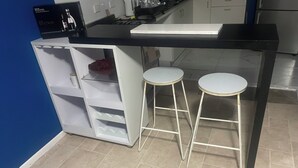 Une cuisine avec un plan de travail noir, des armoires blanches et deux tabourets de bar blancs.