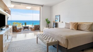 Quarto moderno com uma cama grande, uma TV e varanda com vista para o oceano.