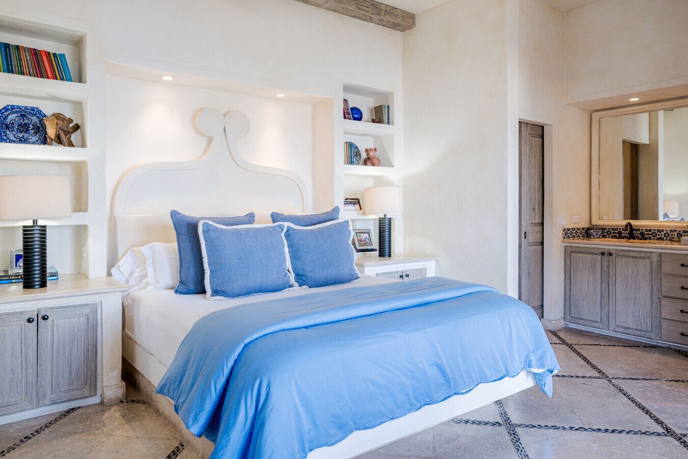 A modern bedroom with a bed, bedside tables, a nightstand, a dresser, a mirror, and built-in shelves with books and decorative items.