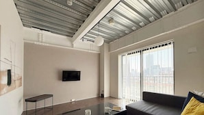 A modern living room with a sofa, a coffee table, a TV mounted on the wall, and large windows with a city view.