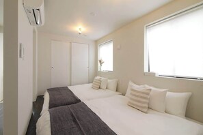 A hotel room with two beds, a window, and a door.