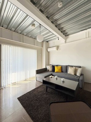 A modern living room with a sectional sofa, a coffee table, and a large window with blinds.