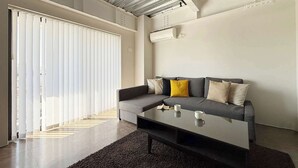 A modern living room with a grey sofa, a black coffee table, and a large window with blinds.
