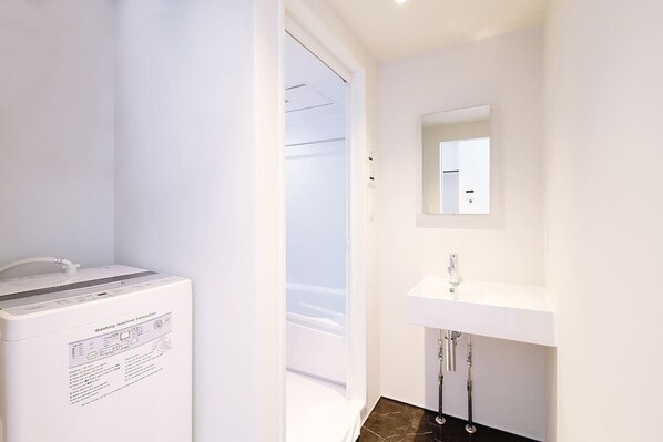 A bathroom with a washing machine, a sink, and a mirror on the wall.