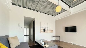 A modern living room with a grey sofa, a glass coffee table, and a minimalist art piece on the wall.