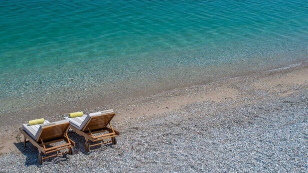Una playa con dos sillones de madera y una toalla amarilla, frente a un mar azul y transparente.