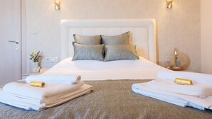 Una cama bien hecha con almohadas, dos lámparas fijadas a la pared y toallas dobladas en el suelo.