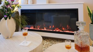 Una sala de estar moderna con chimenea, un jarrón de flores y un vaso de whisky sobre una mesa redonda.