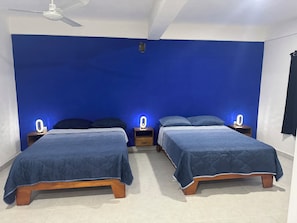 A room with two beds, each with a wooden frame and blue bedding. There are bedside tables with illuminated wall sconces.