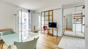 A modern living room with a glass table, two chairs, a TV on a stand, and a view of the city through large windows. - The cellarman  Pathéon by Mon Mon Petit Faré (Paris)