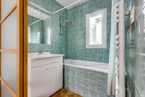 Une salle de bain avec un meuble-lavabo blanc, une baignoire et une fenêtre.