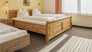 A bedroom with a wooden bed, a nightstand, a vase with flowers, a wall-mounted lamp, and a window with sheer curtains. - Large holiday apartment, 200m to the ski bus (Fieberbrunn)