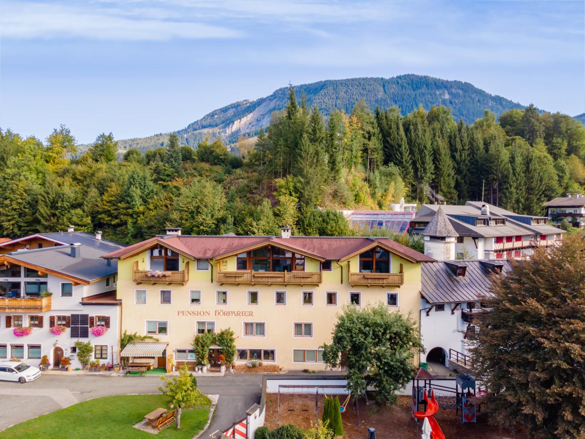 A pension hotel with multiple floors, balconies, and a view of a forested mountain.