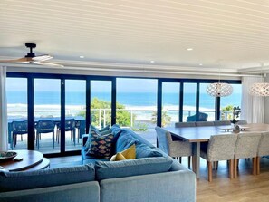 A spacious room with a large sliding glass door leading to a balcony with a view of the ocean. There is a sofa, a dining table, and chairs. - “The Cottage'' Morgan Bay with breathtaking views (East London)