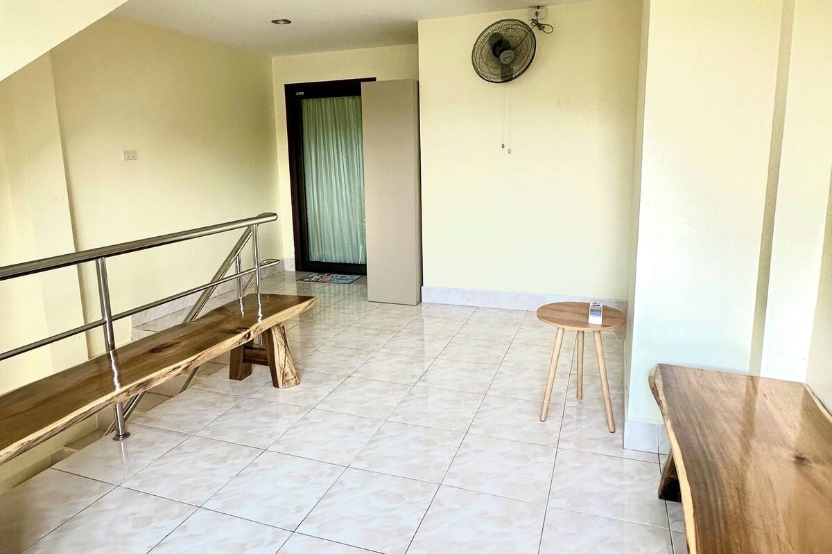 A spacious room with a tiled floor, a wooden bench, a small stool, and a staircase with a metal railing.