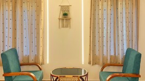Une pièce comprenant deux fauteuils turquoise, une table basse avec un plateau en verre et des rideaux à motifs floraux.