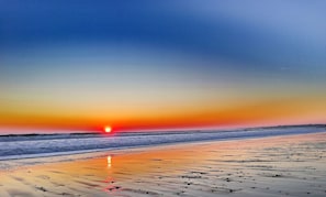 Uma praia ao pôr do sol, com ondas e céu claro.
