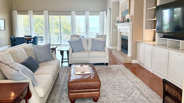 A spacious living room with a sofa, ottoman, and a flat-screen TV.