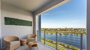 A balcony with wicker furniture, a view of a lake, and a grassy area.