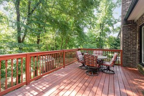 A wooden deck with a red railing, surrounded by trees, and a brick building to the right. - Spacious Mid Term Rental! University City Home with Game Room, Huge Fenced Yard, Pets OK +20% Off! (Charlotte)