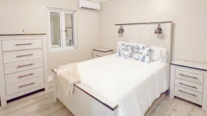 Un dormitori amb un llit, dues tauletes de nit, un prestatge i un ventilador de sostre, a més d'una unitat de climatització.
