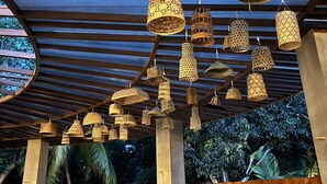 A covered outdoor area with hanging woven light fixtures and tables and chairs underneath. - Hotel Dumaguete (Dumaguete)